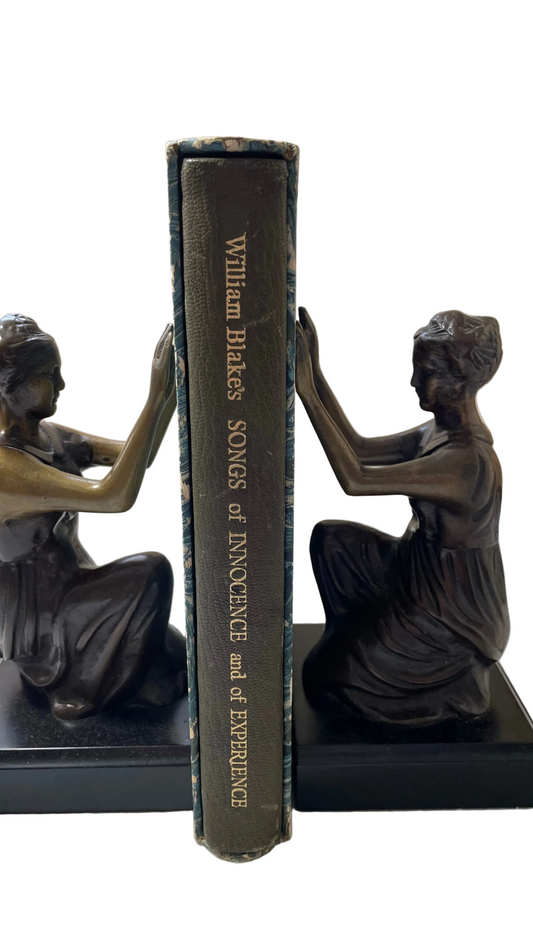 Dark gilt-lettered spine of William Blake’s Songs of Innocence and of Experience inside its worn marbled slipcase, between figurative bookends.