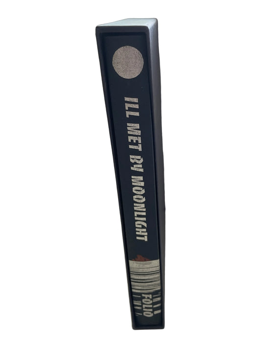 Spine of Ill Met by Moonlight in its dark slipcase, with cream lettering, a circular motif and horizontal lines near the foot.